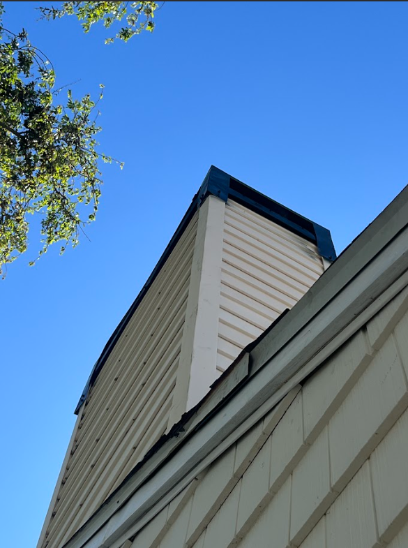 Close-up of a house corner with white siding, blue trim, and a clear blue sky background.