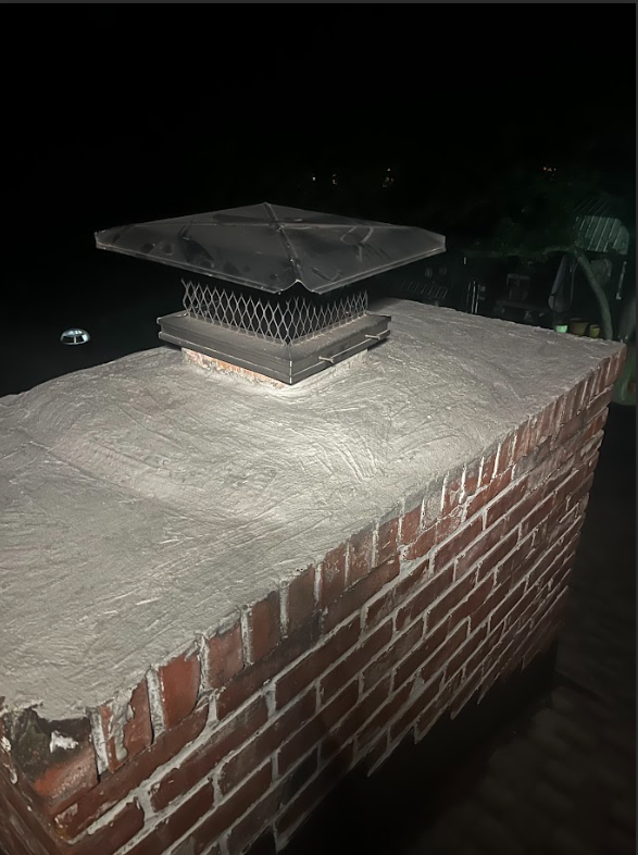 Brick chimney with a metal cap on a dark night.