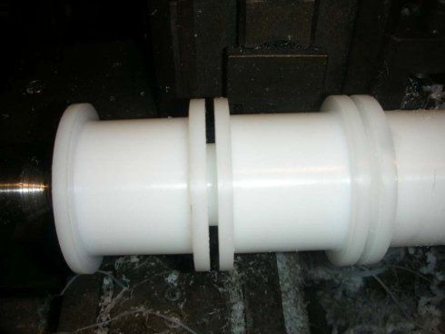 Parti cilindriche in plastica bianca con anelli neri, su una superficie metallica.