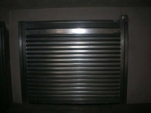 Porta di sicurezza avvolgibile in metallo, chiusa. Installata in una parete, in un ambiente buio.