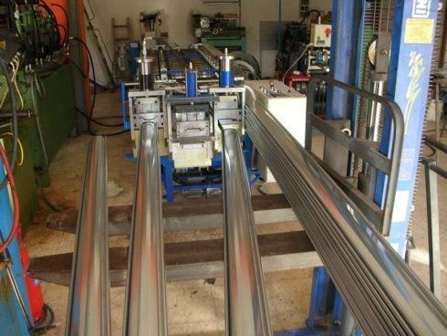 Macchina per la formatura dei metalli con lunghi tubi argentati in un ambiente da officina.