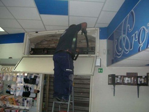 Una persona su una scala pulisce un'unità di aria condizionata all'interno di un negozio.