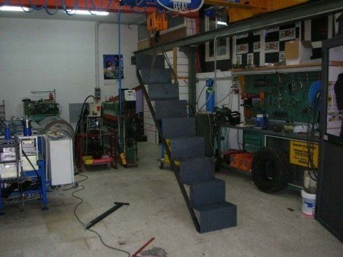 Scala metallica che conduce al soppalco di un'officina. Gradini grigi e struttura nera.