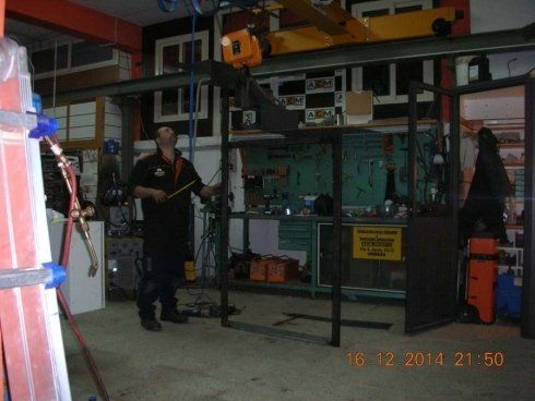 Uomo in un'officina con in mano un attrezzo per la saldatura, in piedi vicino a una struttura metallica.