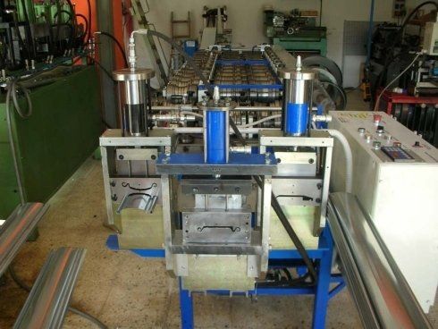 Macchina industriale con componenti blu, argento e trasparenti, probabilmente per la formatura dei metalli, in un ambiente di officina.