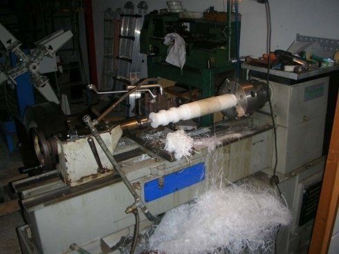 Un tornio che lavora un oggetto cilindrico bianco, producendo trucioli bianchi. Impostazione di un'officina meccanica.
