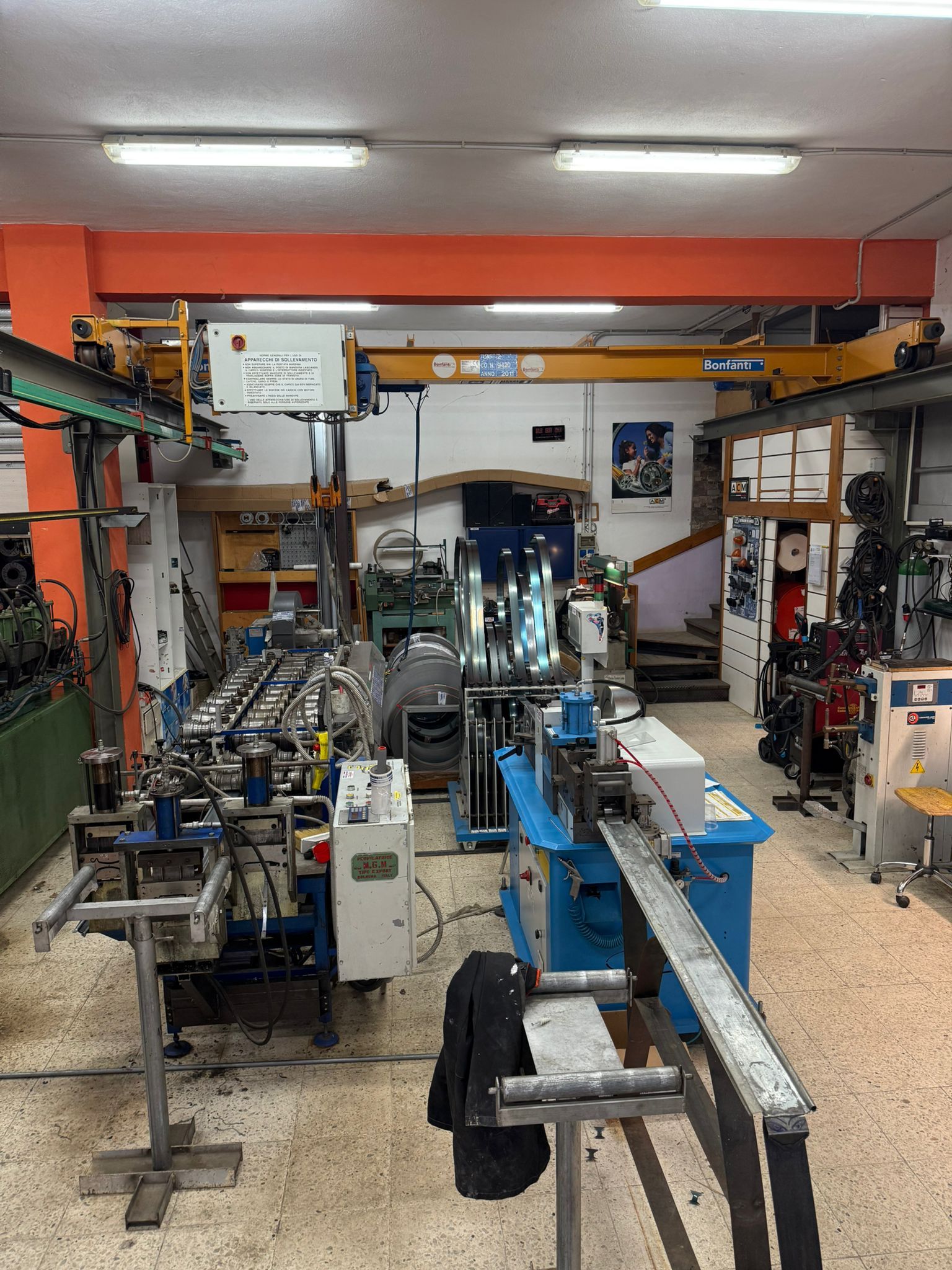 Officina con macchinari industriali: piegatubi, attrezzatura per la lavorazione dei metalli, carroponte, illuminazione fluorescente.