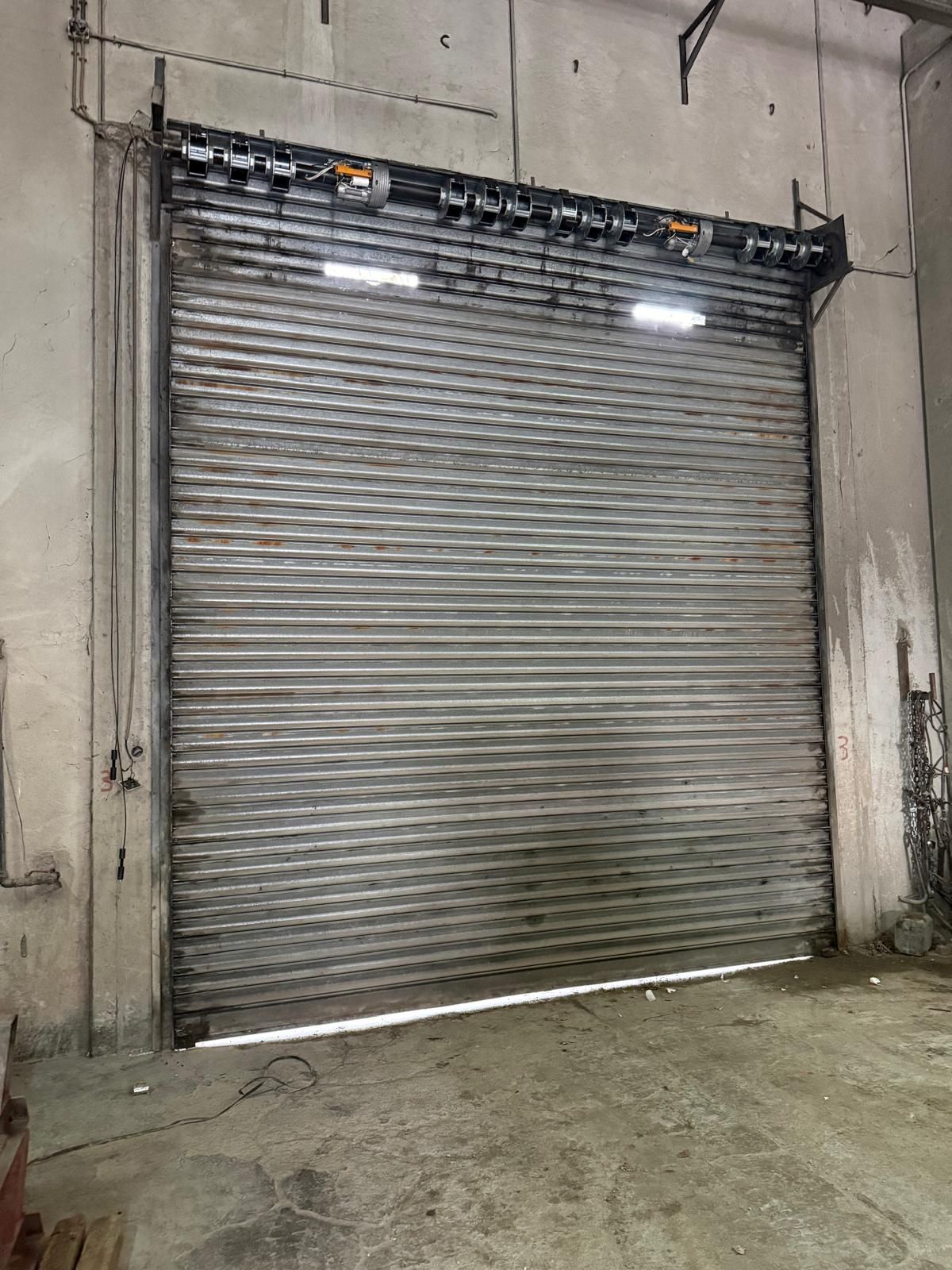 Porta di sicurezza metallica avvolgibile, chiusa in un edificio in cemento.