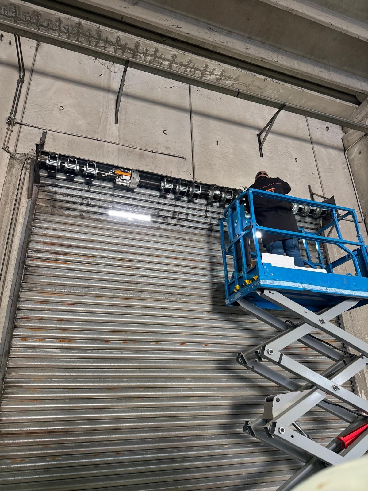 Persona su un ascensore che lavora su una porta avvolgibile metallica da garage in un magazzino.