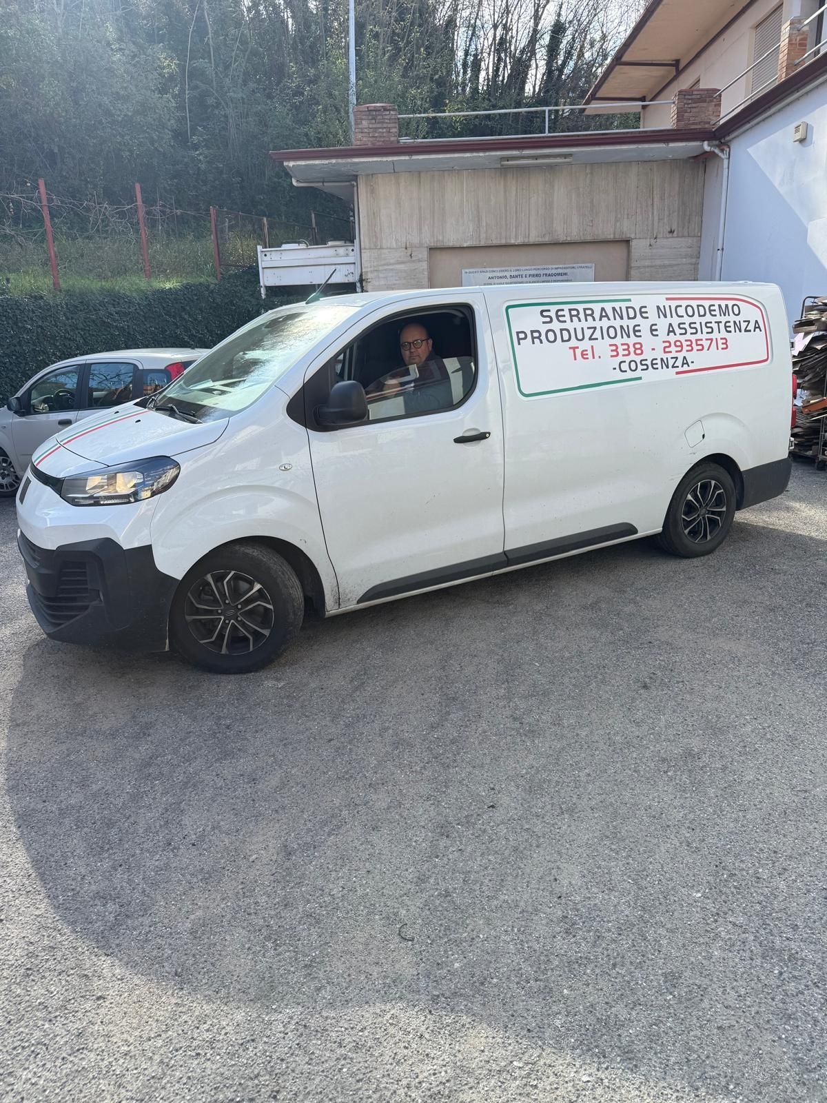 Furgone bianco con scritta sulla fiancata, parcheggiato in un parcheggio. Una persona è seduta al posto di guida.