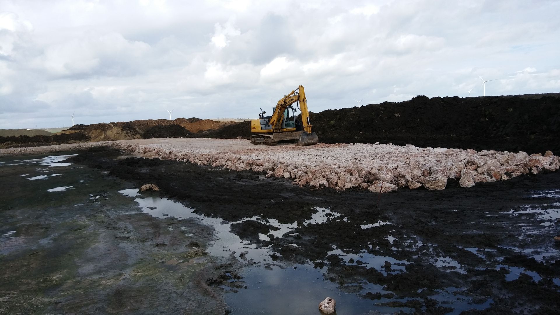 Un escavatore giallo sta lavorando su un grande mucchio di terra
