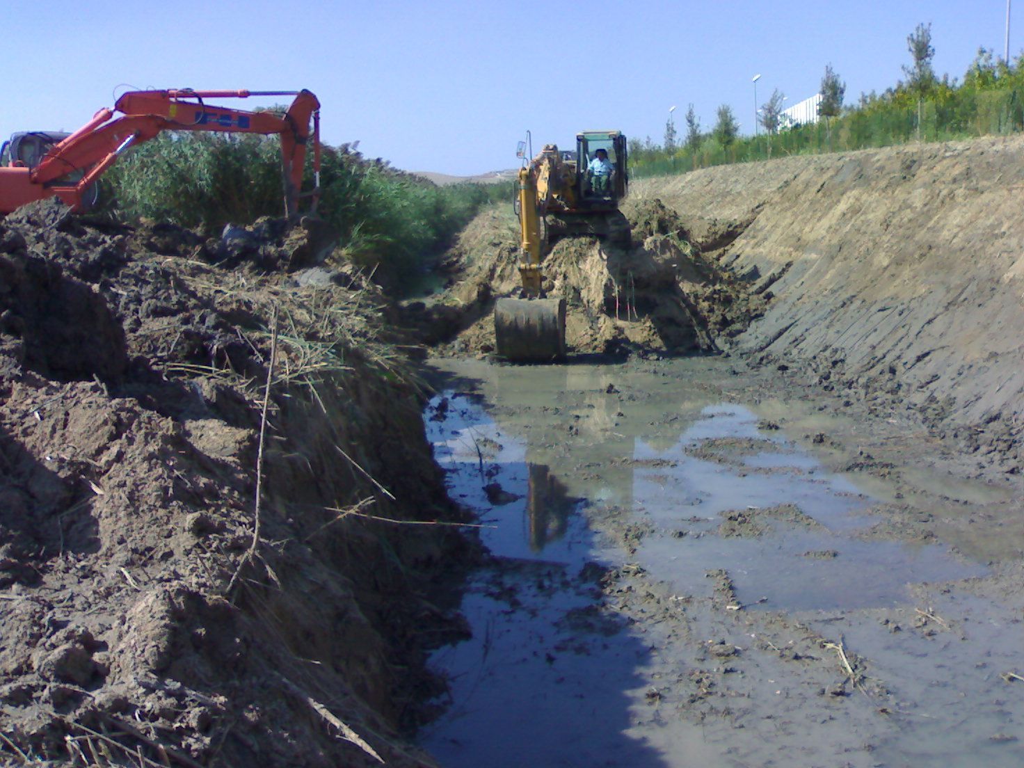 Un grande escavatore arancione sta scavando una buca nel terreno