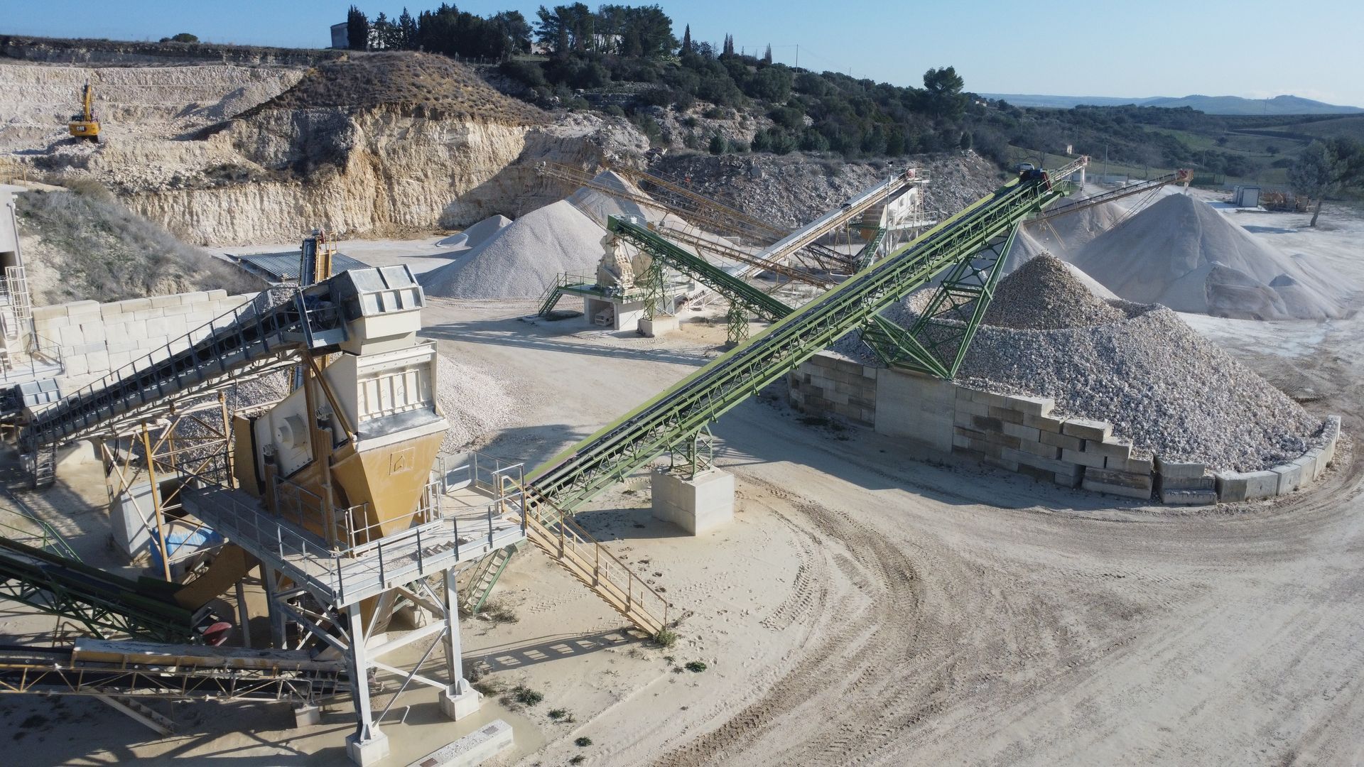 Una vista aerea di una grande cava di roccia con un nastro trasportatore.
