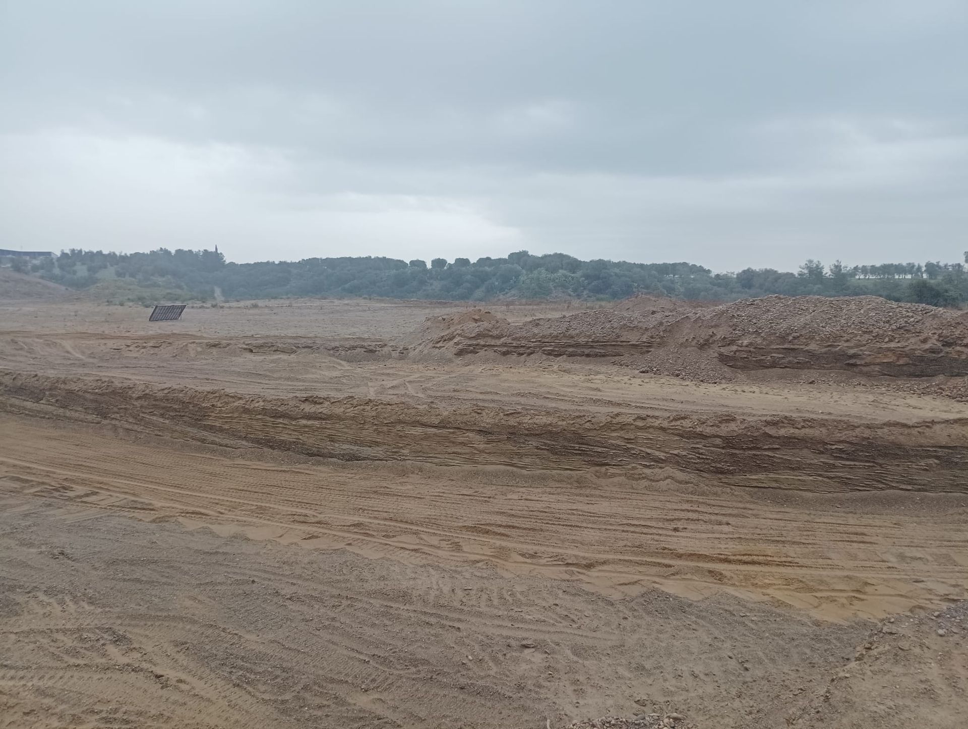 Un grande campo sterrato con alberi sullo sfondo in una giornata nuvolosa