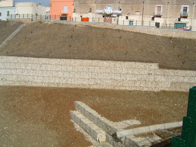 Un muro di mattoni circonda un campo di terra con edifici sullo sfondo