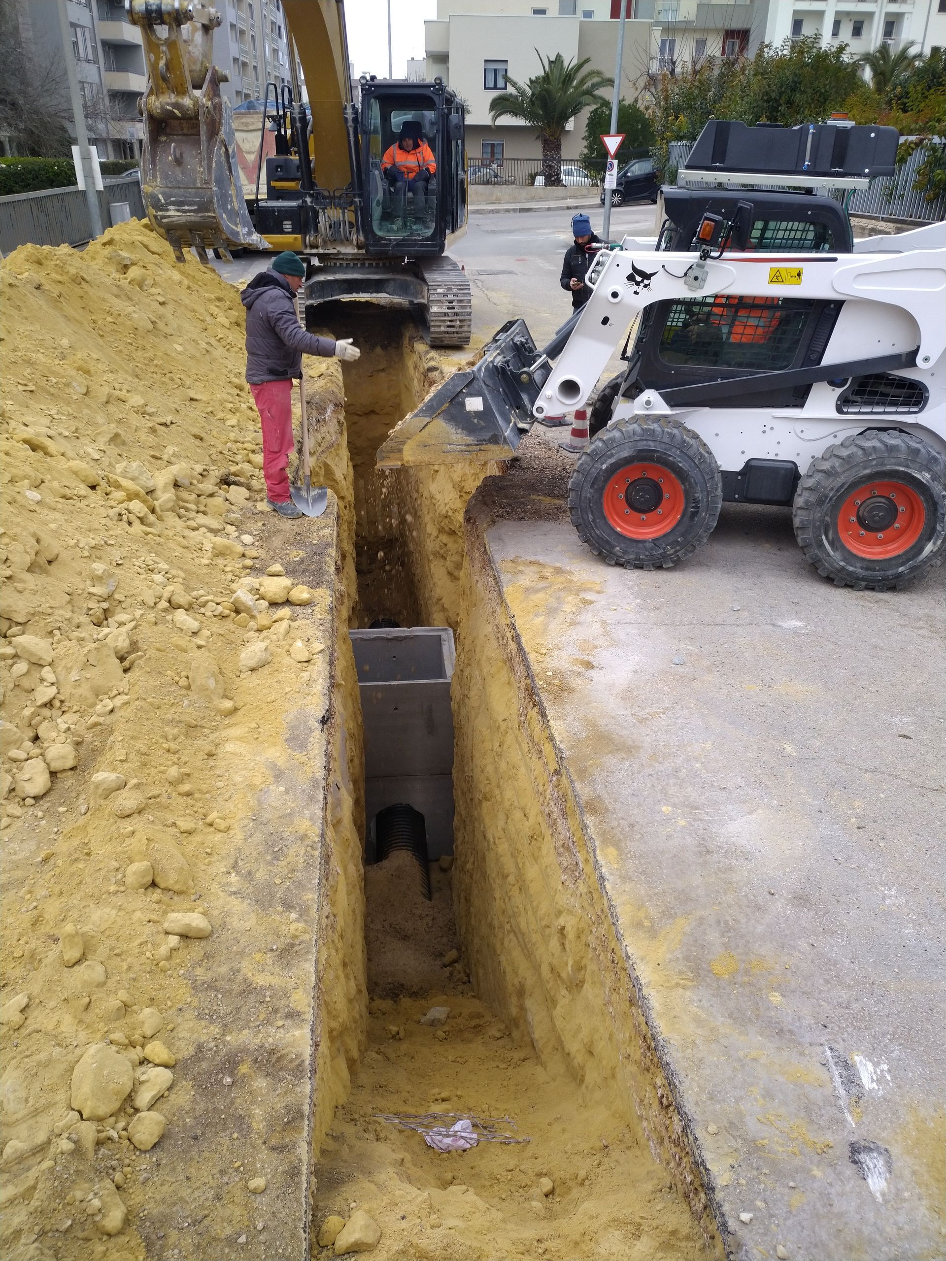 Un uomo sta scavando una buca nel terreno accanto a una ruspa.