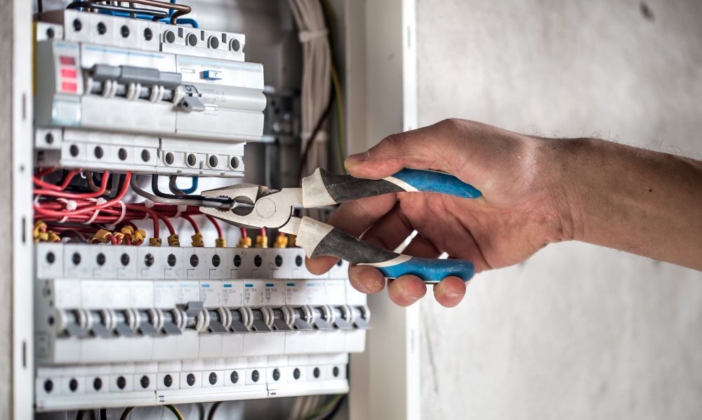 Hand using pliers on electrical panel wiring.