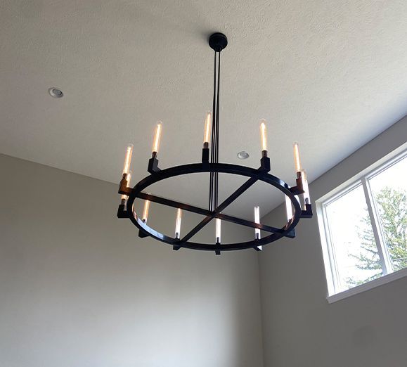 Black circular chandelier with ten lights hanging from a white ceiling, next to a window.