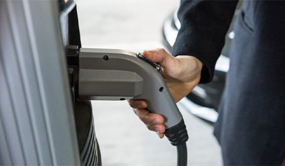 Hand plugging an electric vehicle charger into a car's charging port.
