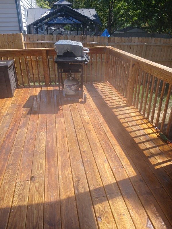 A wooden deck with a grill on it and a fence in the background.