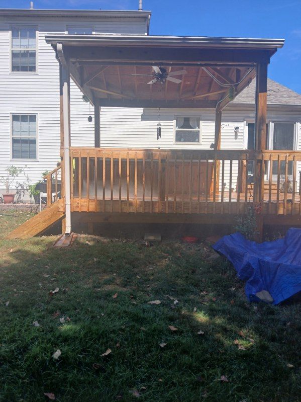 A wooden deck with a gazebo attached to it is in the backyard of a house.