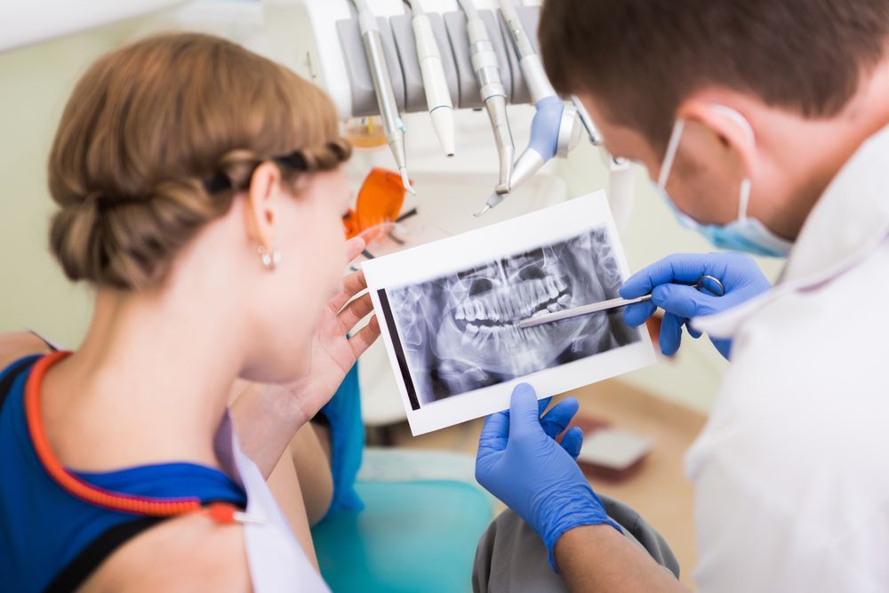 A Dentist is Looking at an X-ray of a Patient 's Teeth — Graham Johnson Dental Surgery In Beresfield, NSW