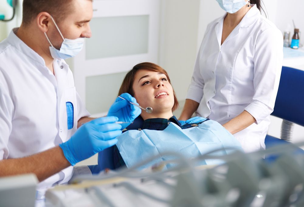 A Woman is Sitting in a Dental Chair While a Dentist Examines Her Teeth — Graham Johnson Dental Surgery In Beresfield, NSW