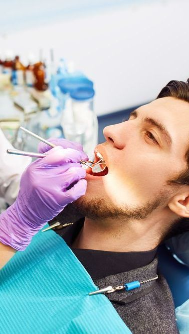 A Man is Getting His Teeth Examined by a Dentist — Graham Johnson Dental Surgery In Beresfield, NSW