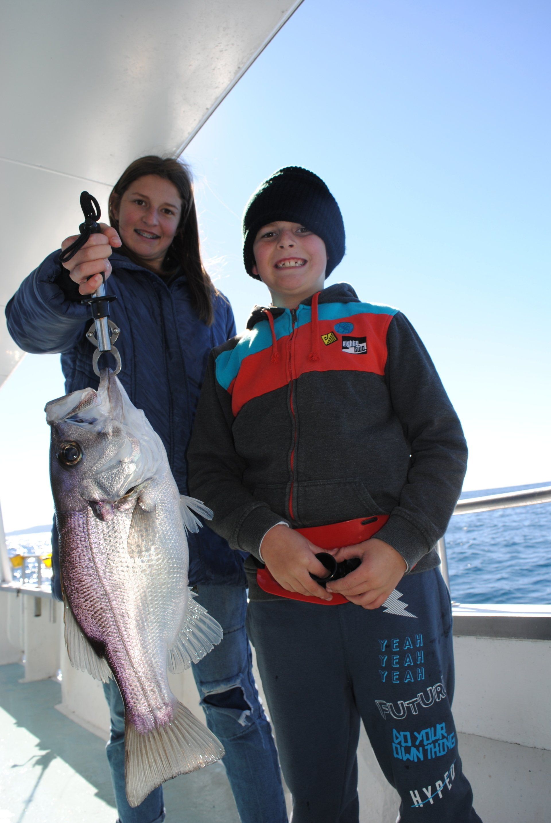 A boy and a girl holding a large fish on a boat