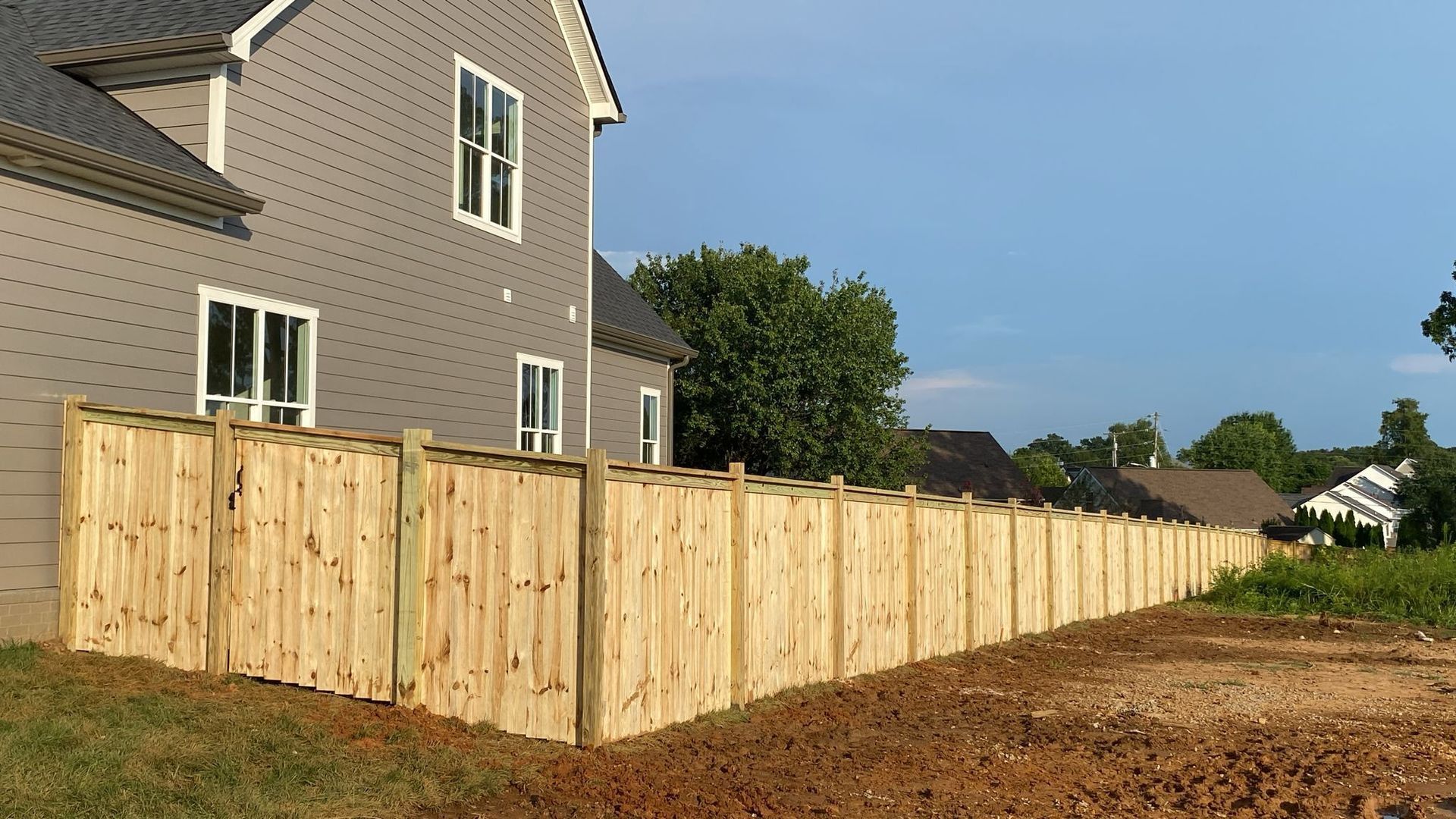 Wooden fence alongside a grey house on a sunny day.