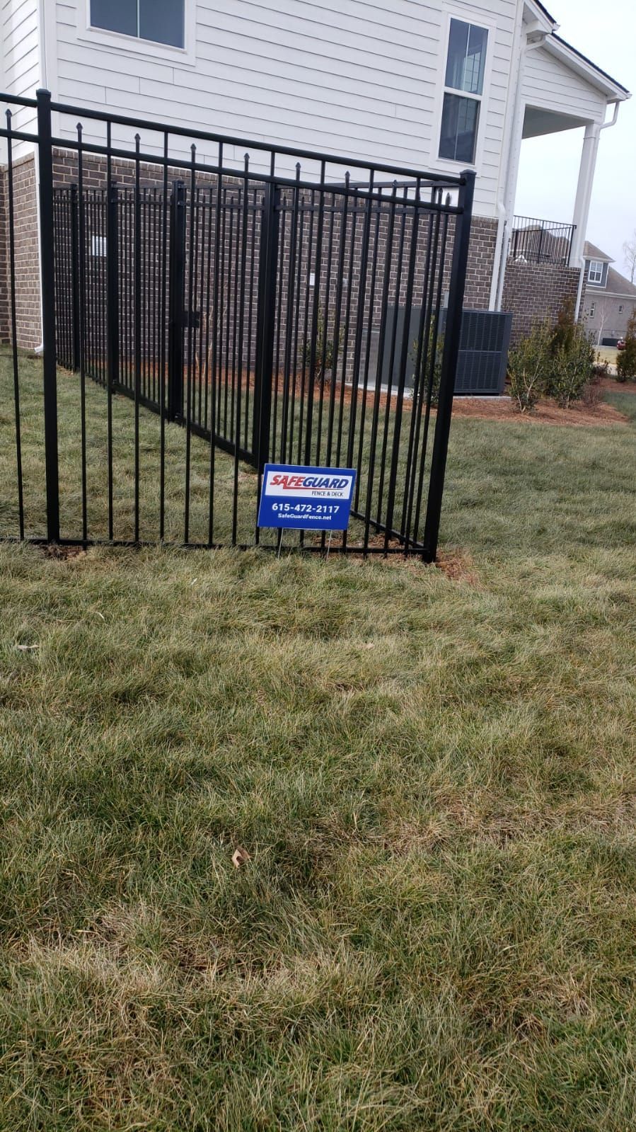 Black metal fence in a grassy yard, with a house in the background.