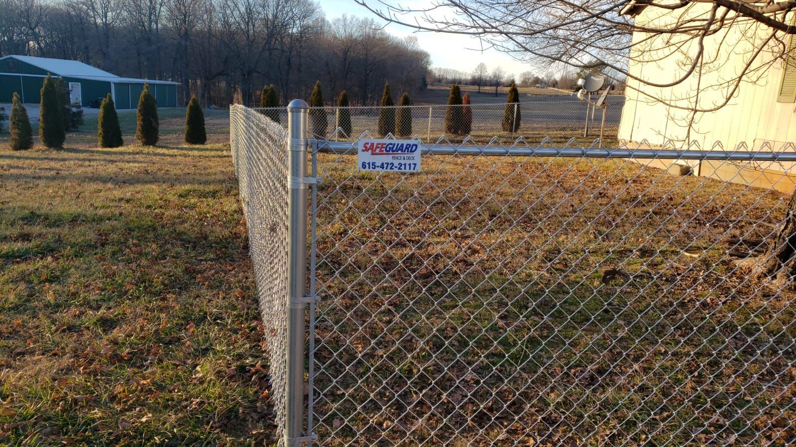 Chain link fence in grassy field, with trees and building in background.