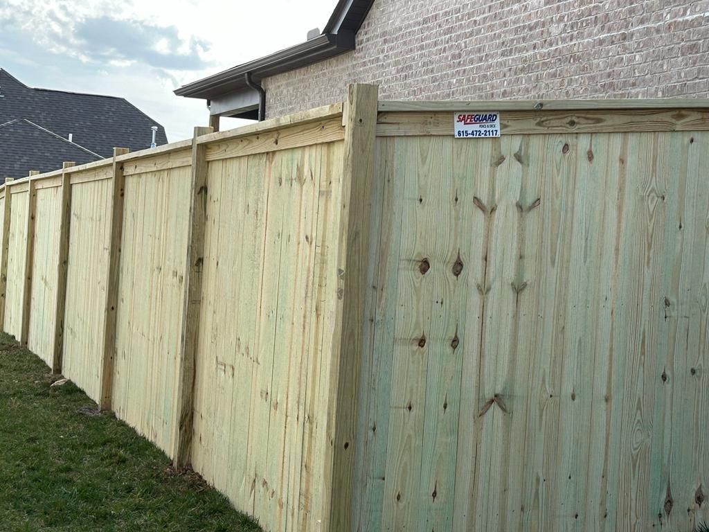 Wooden privacy fence along grass with a brick wall background.
