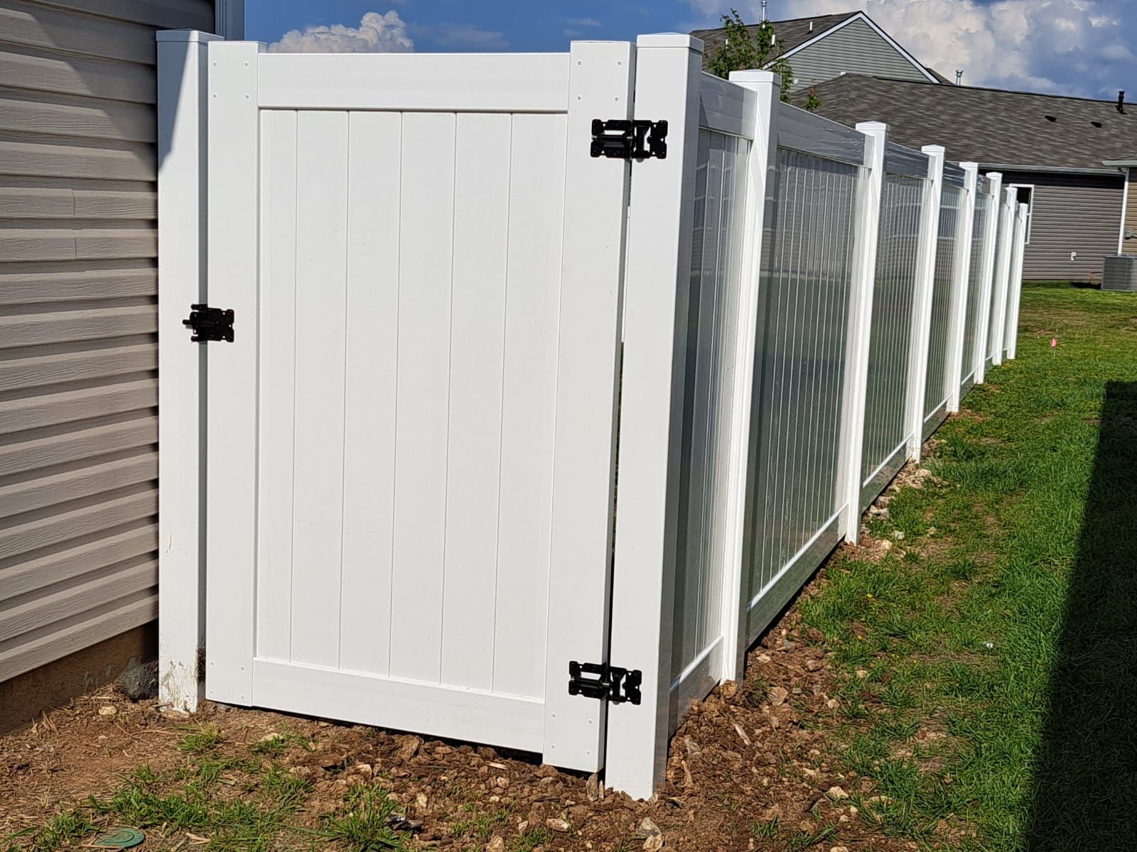 White vinyl gate and fence in front of a house, black hardware, set in a grassy yard.