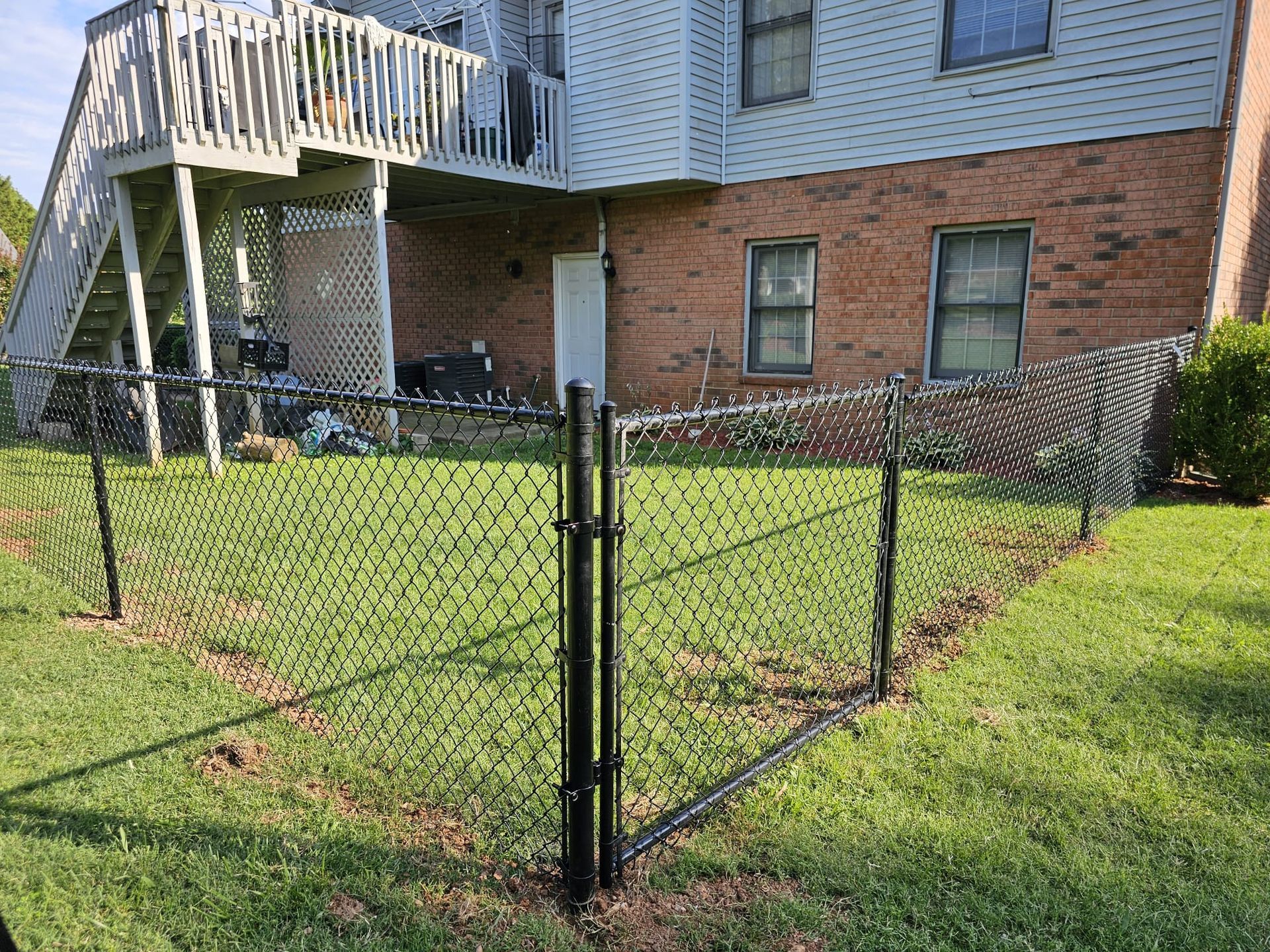 Black chain-link fence surrounds a small green yard next to a brick building with a wooden deck.