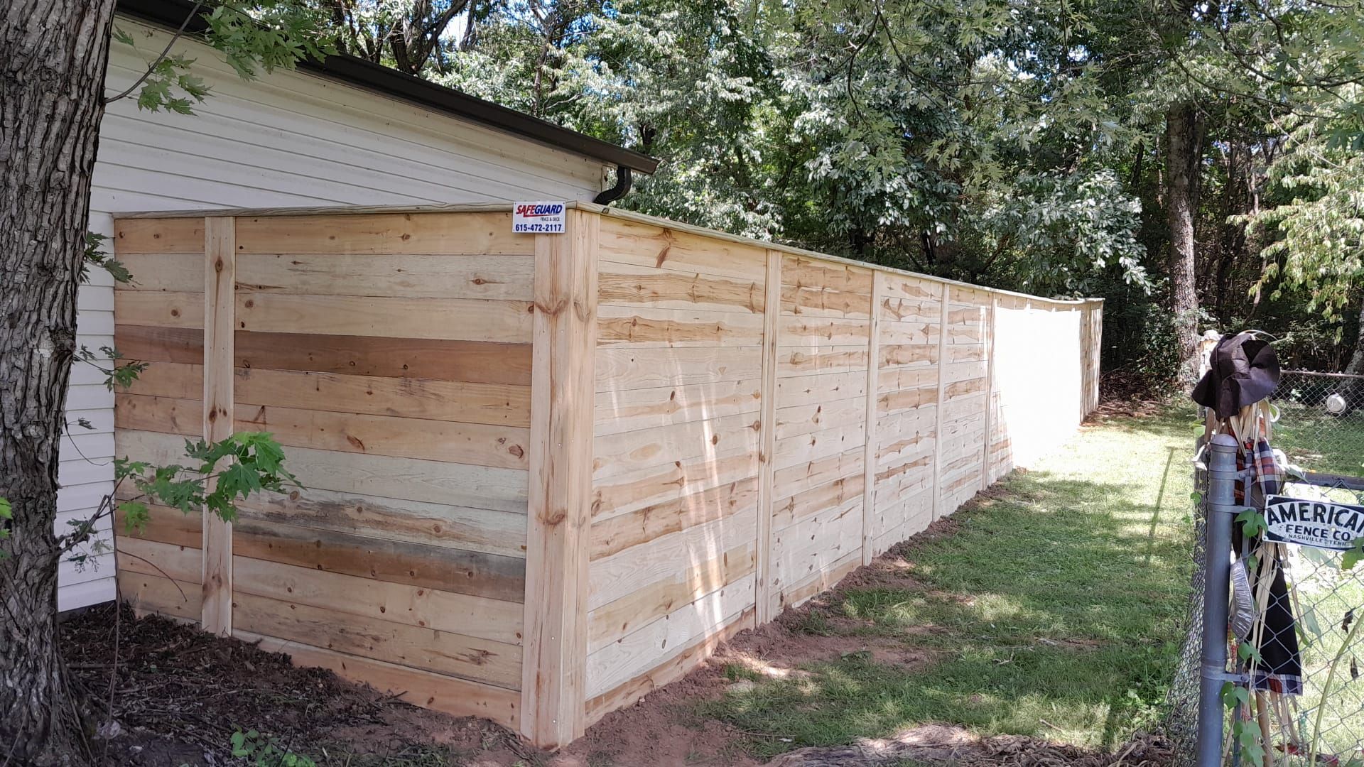 Wooden fence along a building, on a grassy lawn with trees in the background.