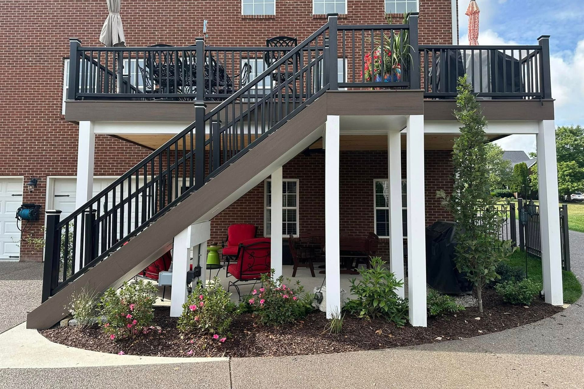 Two-story deck with stairs, black railing, brown decking, white columns, and landscaping.