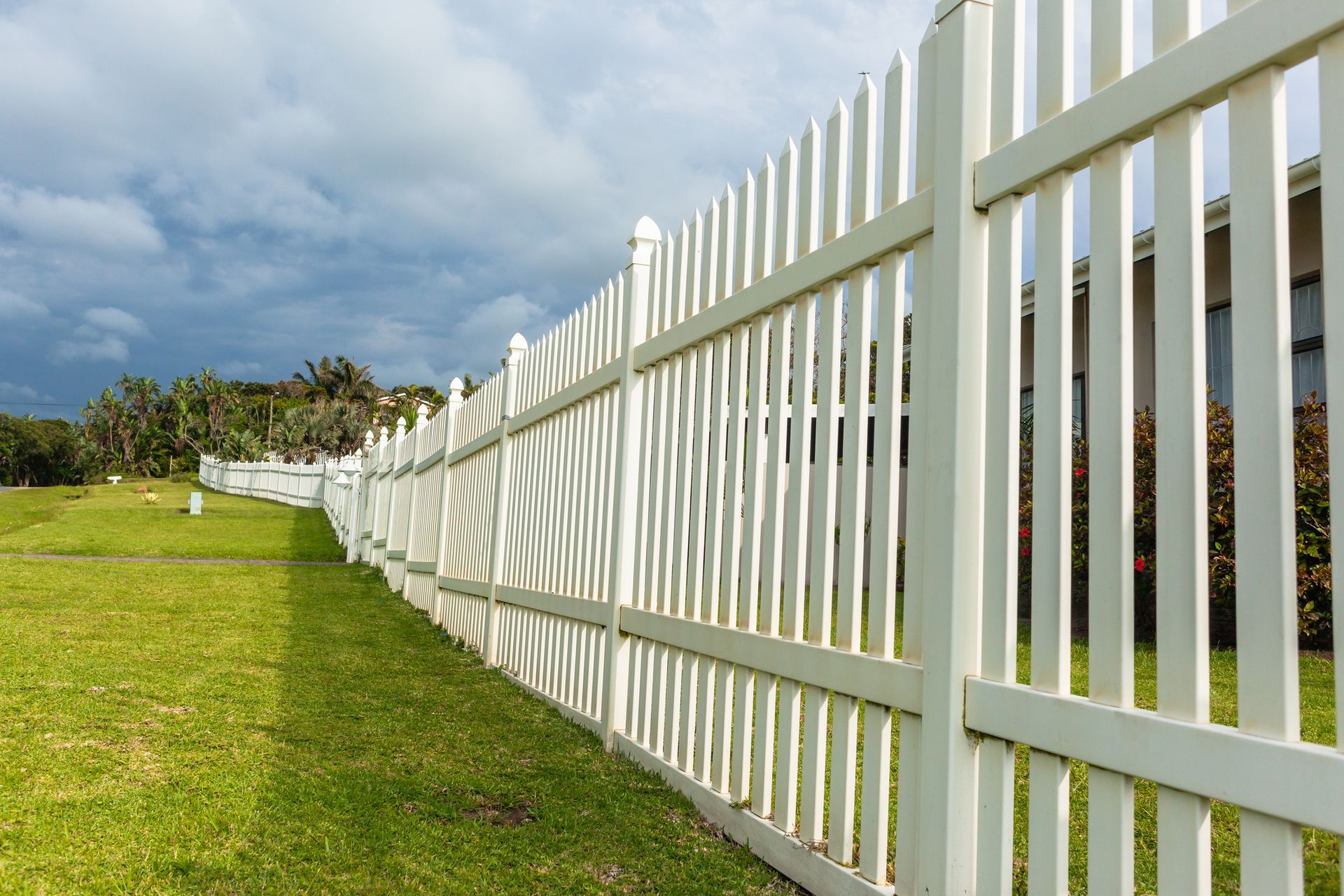 White picket fence along a grassy lawn, under a cloudy sky.