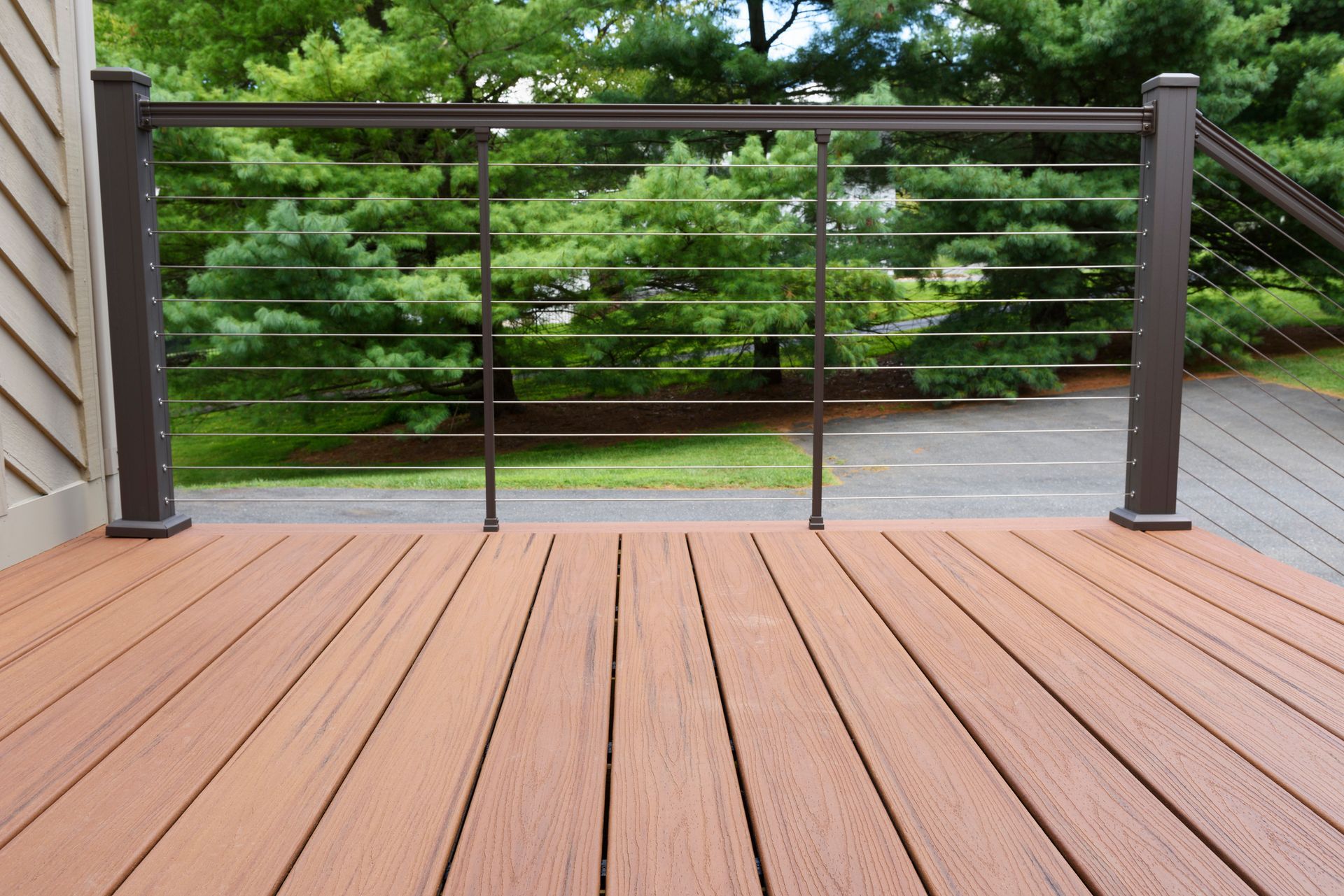 Composite deck with brown railing and cable infill, overlooking a green yard.