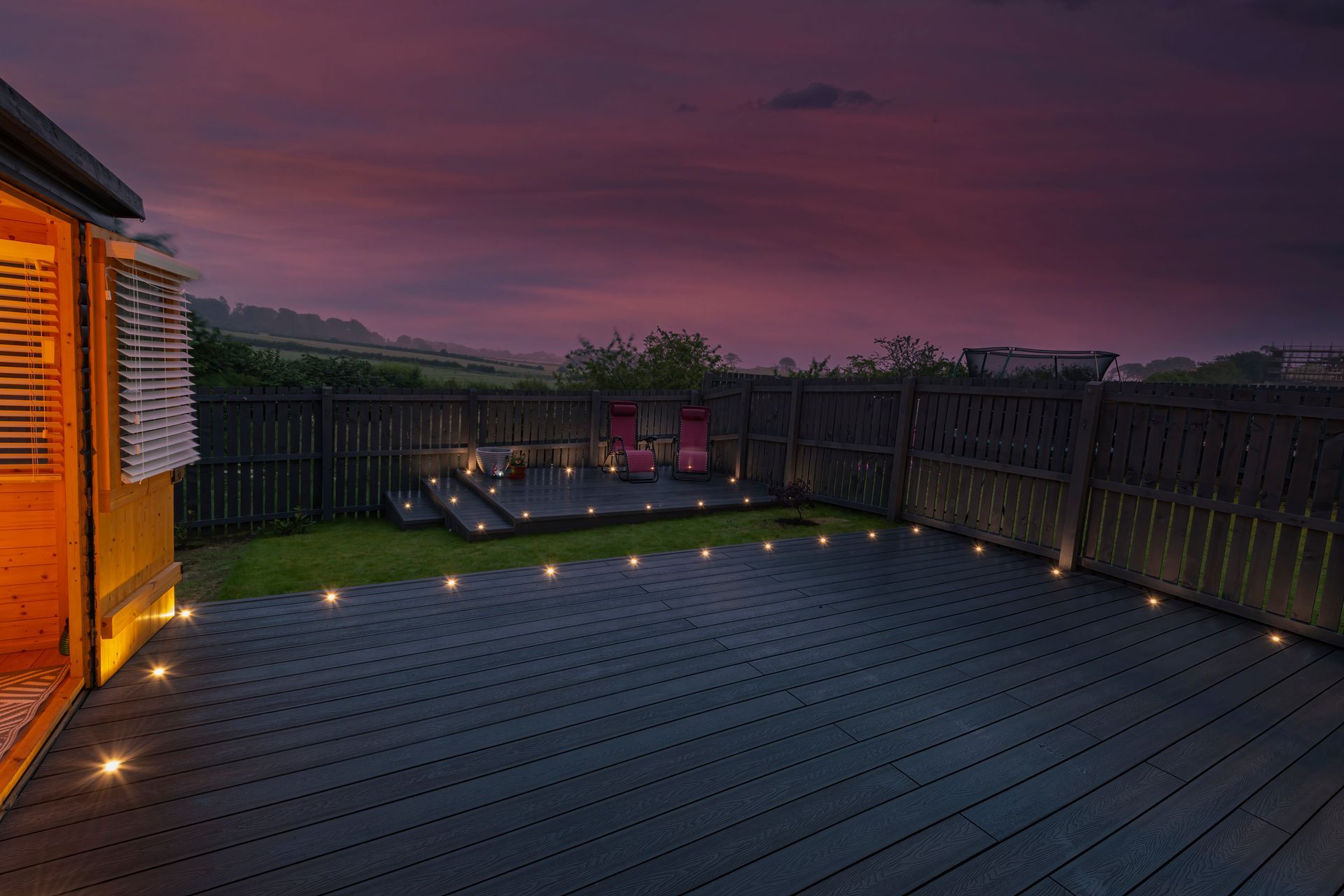 A dark deck with inset lights leads to a raised platform with two chairs, all under a purple dusk sky.