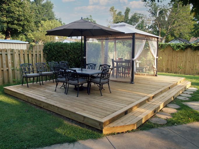 Wooden backyard deck with patio furniture, umbrella, and gazebo.