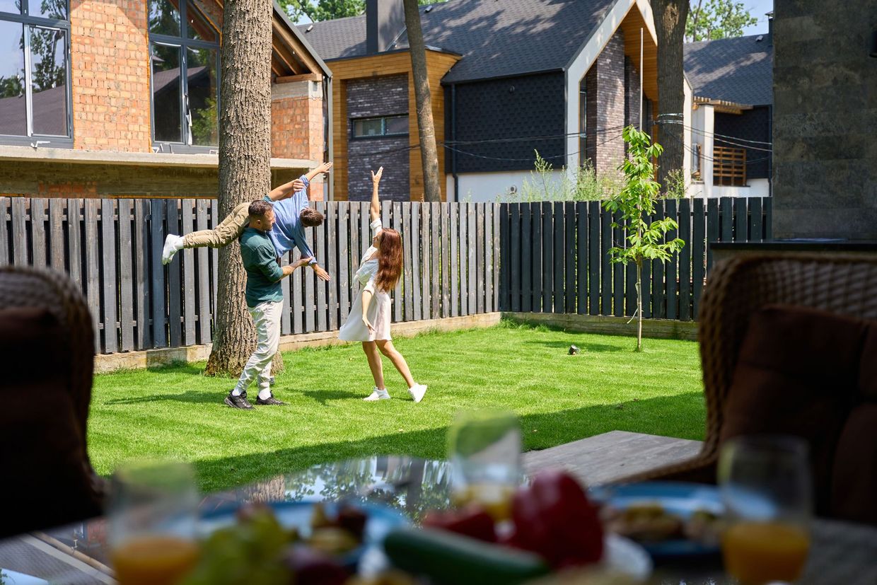 Family playing in backyard with tree, woman and man holding child, sunny day.