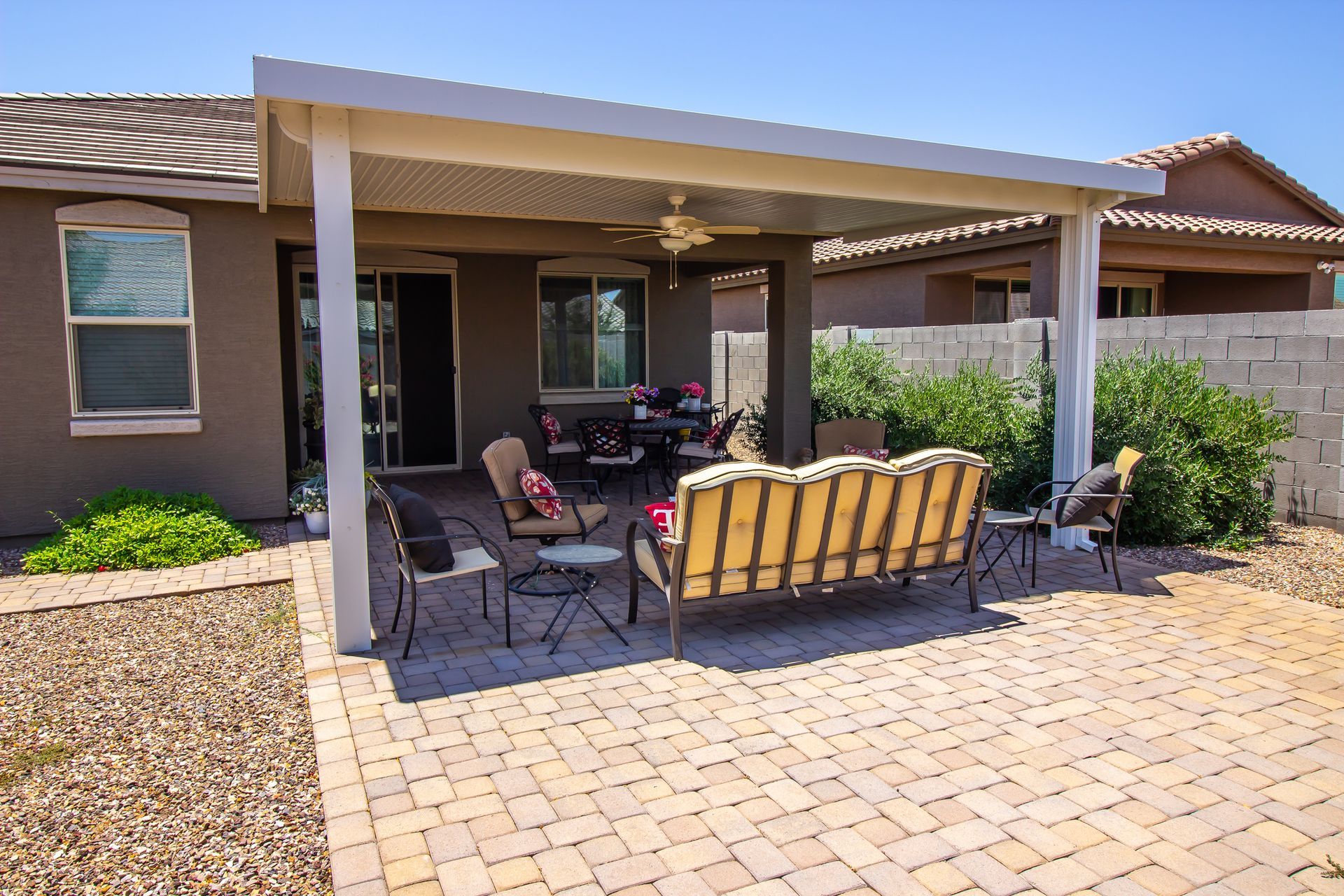 Covered patio with seating: a beige-tiled patio, wooden furniture, and a metal swing under a white, rectangular overhang.