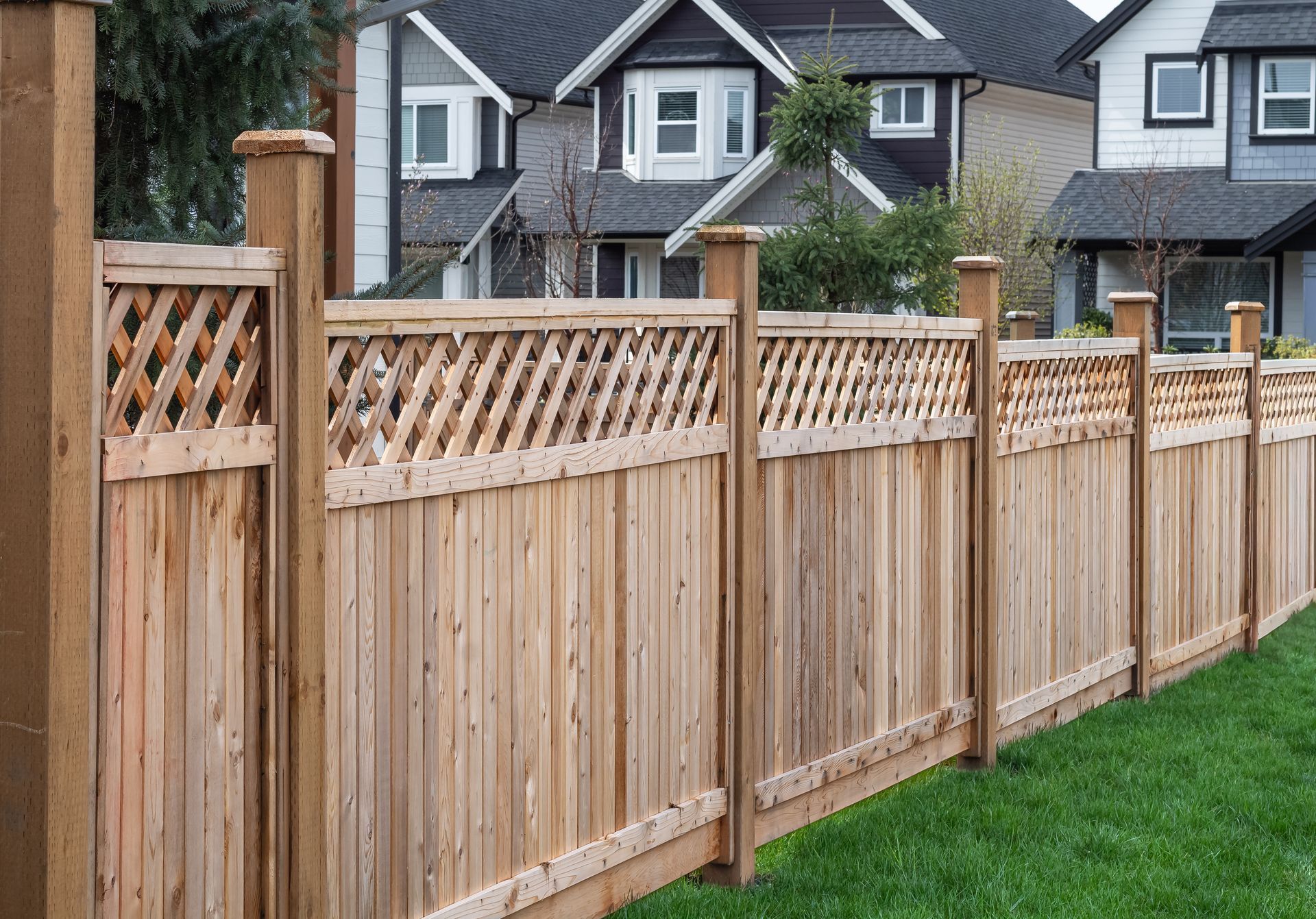 Wooden fence with lattice tops, in front of suburban houses.