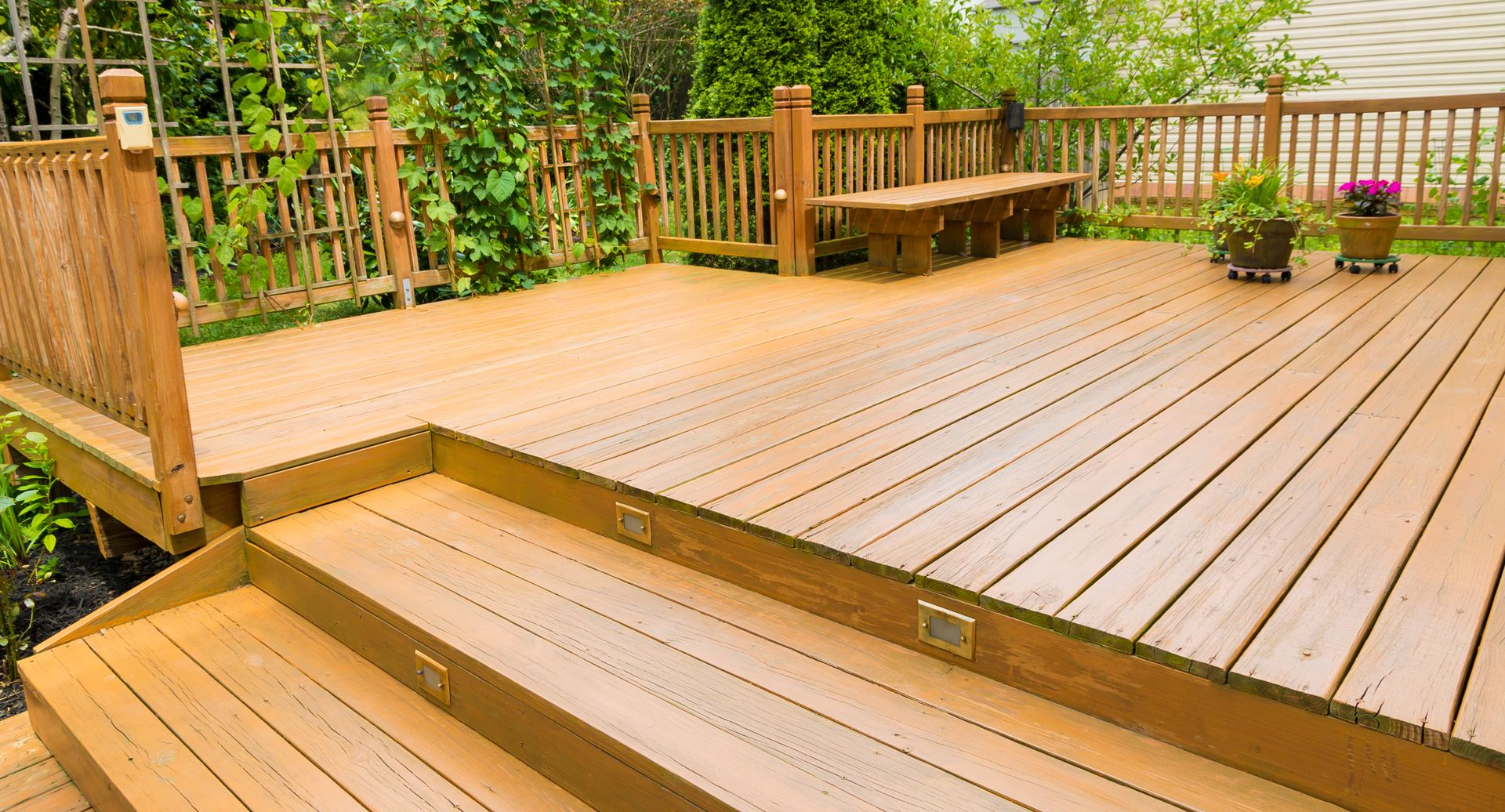Wooden deck with steps, bench, and railings in a backyard setting.