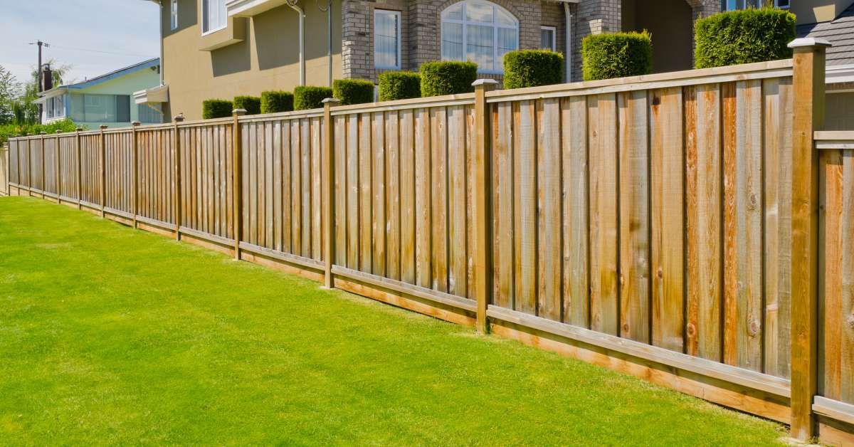 Wooden fence surrounding a green lawn, in front of a house.