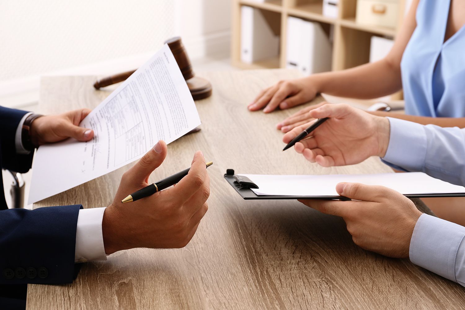 People reviewing documents at a wooden table, one person holding a pen, gavel in the background.