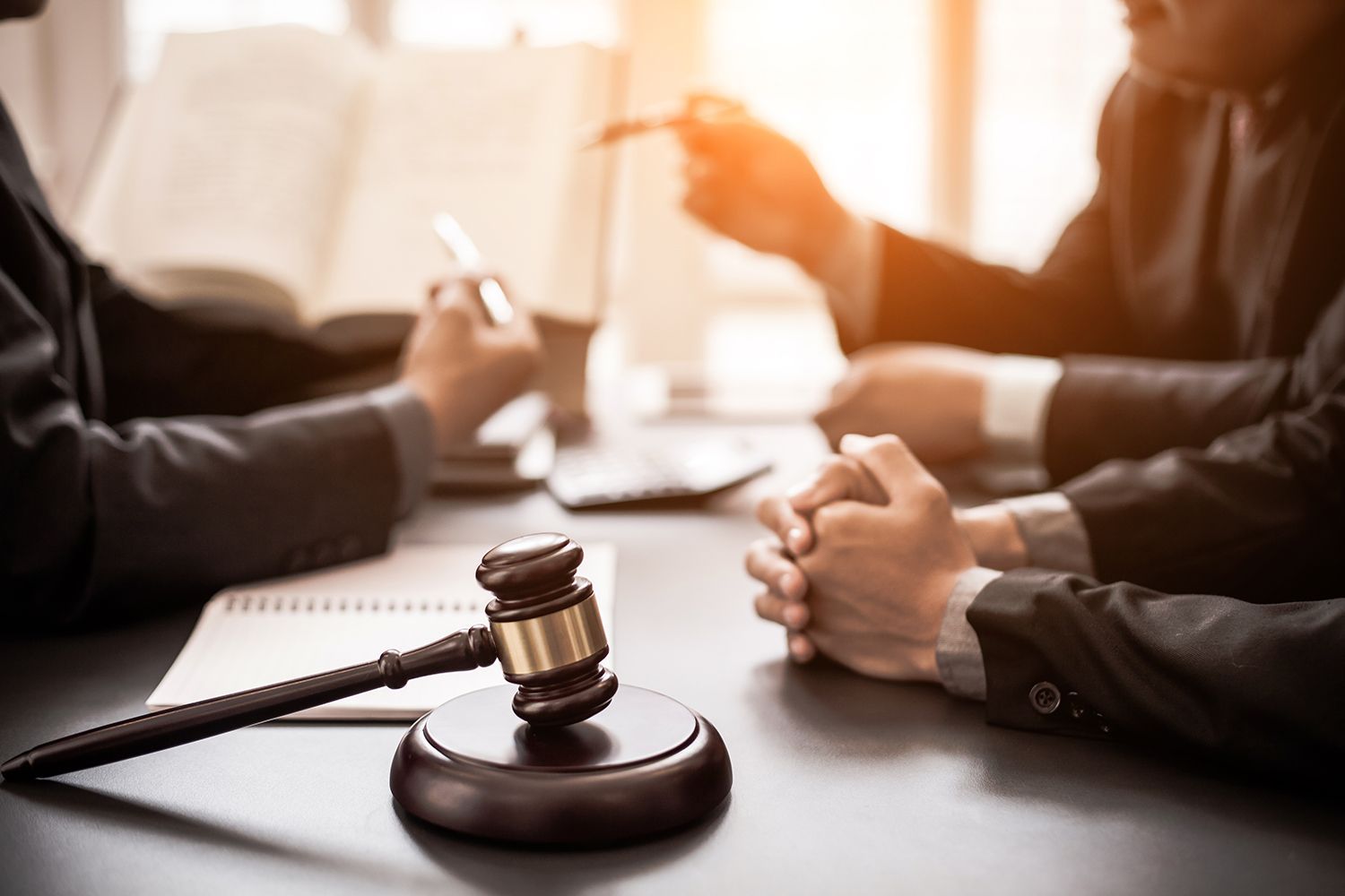 Gavel on a table with lawyers discussing; open book and laptop present.
