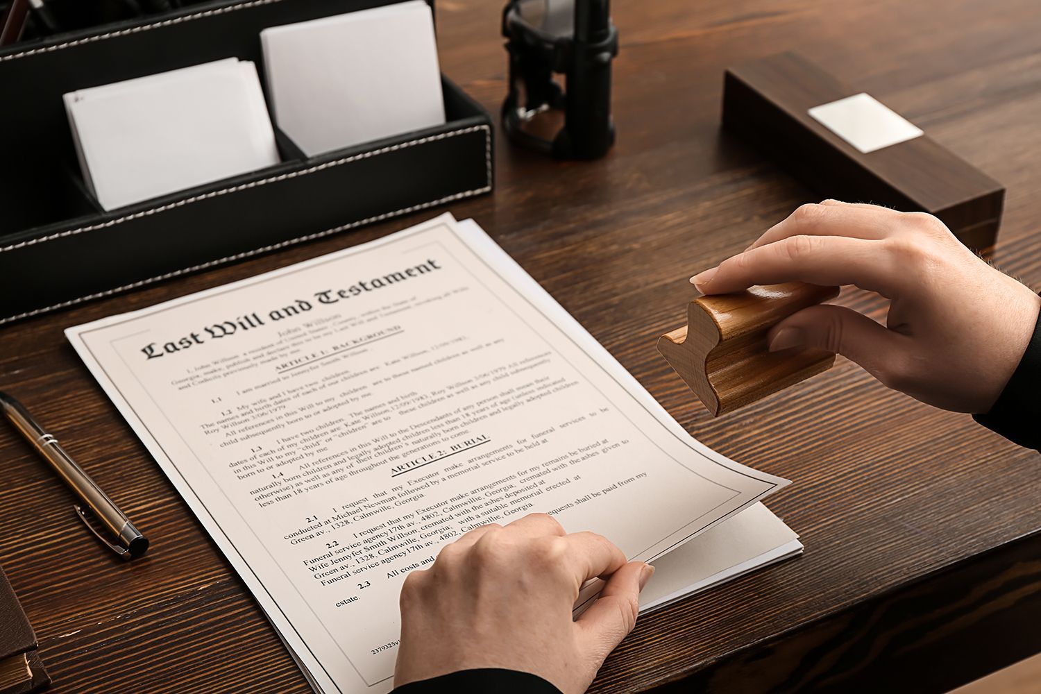 Person signing Last Will and Testament document with a stamp on a wooden desk.