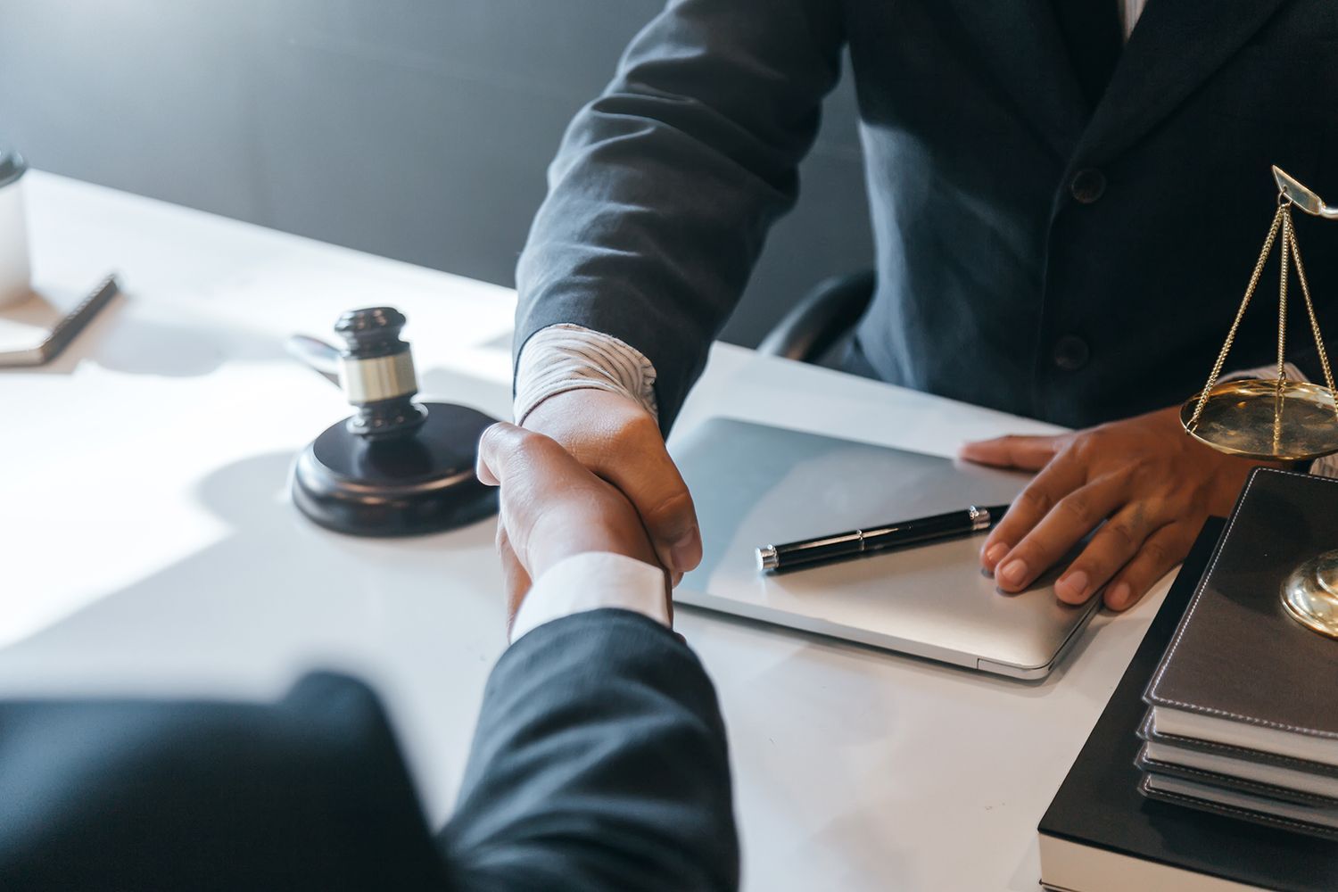 Two people in suits shaking hands over a desk with a gavel and scales of justice. Two people in suits shaking hands over a desk with a gavel and scales of justice.